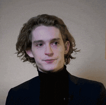 a young man with long hair wearing a black turtleneck and a suit .