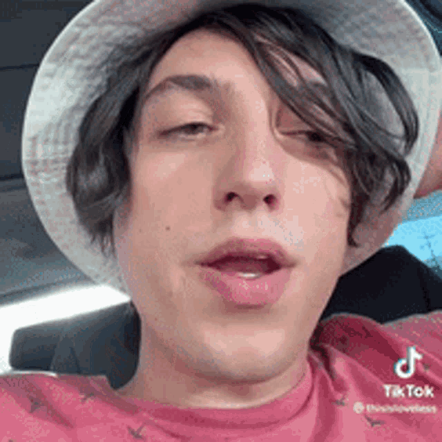 a man wearing a bucket hat and a pink shirt is sitting in a car .