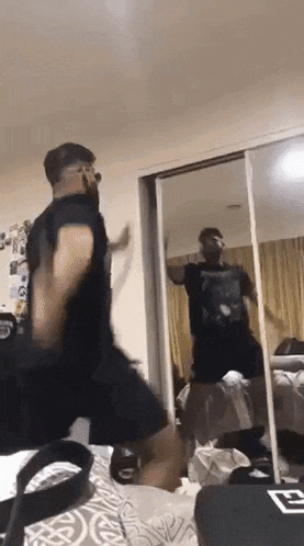 a man in a black shirt is dancing in front of a mirror in a bedroom .