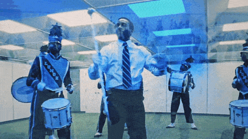 a man in a suit and tie stands in front of a group of marching band members in blue uniforms