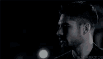 a man with a beard is standing in the dark looking at the camera .