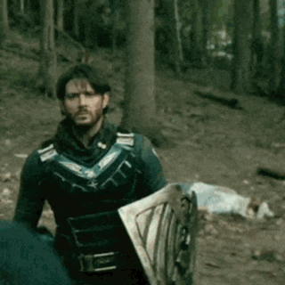 a man in a suit is holding a shield in a forest .