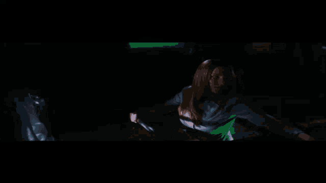 a woman is sitting in a dark room holding a green object