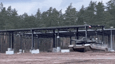a military tank is driving down a dirt road in front of a building in a field .