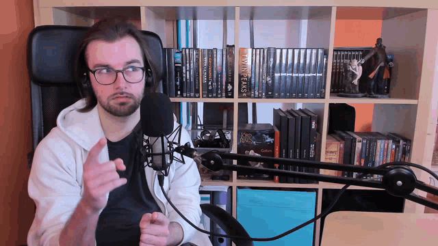 a man sitting in front of a microphone with a bookshelf behind him that has the title twin peaks on it