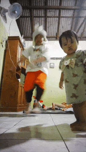 two little girls are jumping in the air in a room with a fan in the background