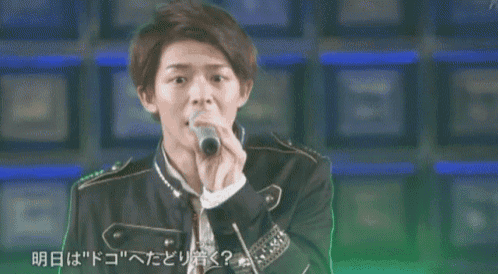 a young man is singing into a microphone while wearing a black jacket and tie