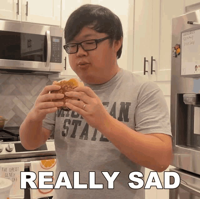 a man wearing a michigan state shirt eating a hamburger