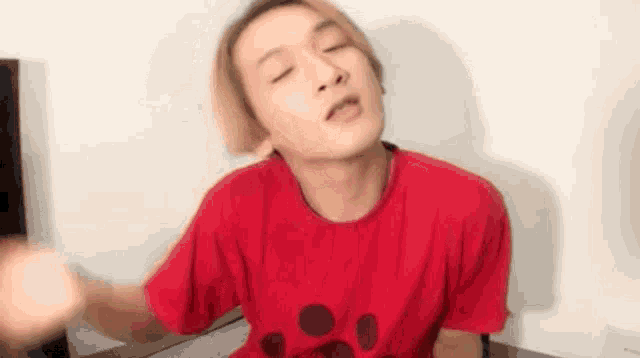 a young man in a red t-shirt is making a funny face with his eyes closed .