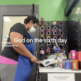 a woman wearing a mask and apron is working in a room with a sign that says `` god on the sixth day '' .