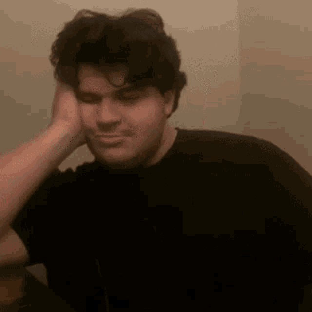 a man in a black shirt is sitting at a table with his hand on his head .