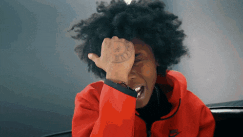 a person wearing a red nike jacket is covering their face with their hand
