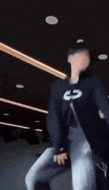a man in a black jacket is dancing in a dark room with lights on the ceiling .