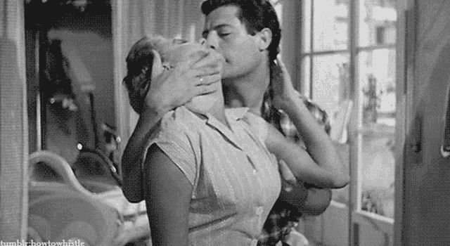 a black and white photo of a man and woman kissing .