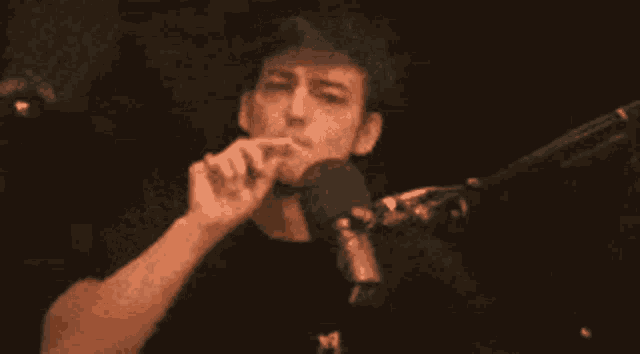 a man is singing into a microphone while sitting in front of a red curtain .