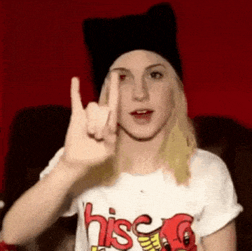 a woman wearing a black cat hat and a white shirt is making a devil horns sign .