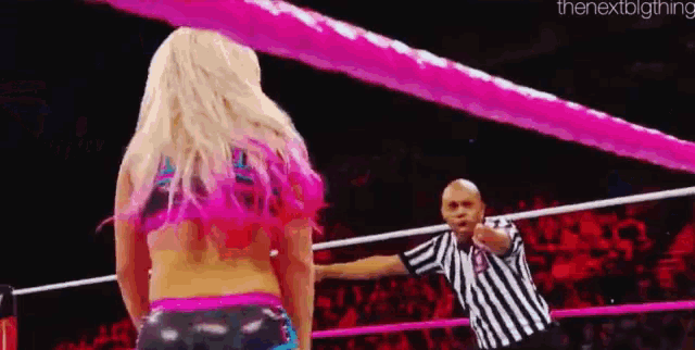 a woman in a pink top is standing in a wrestling ring with a referee .