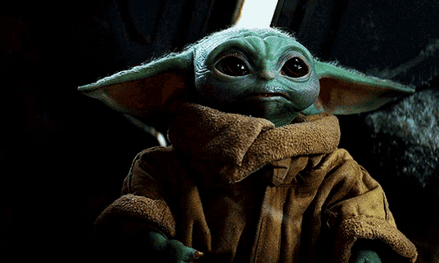 a baby yoda wearing a brown coat and scarf looks at the camera