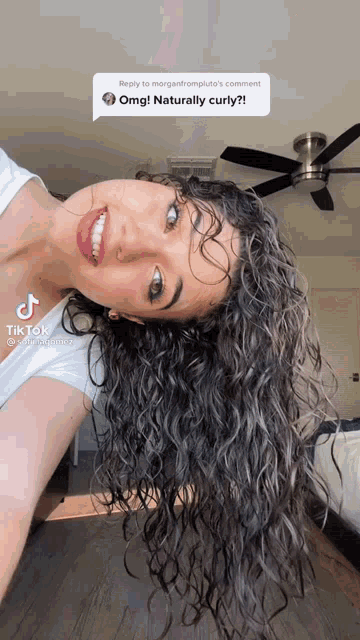 a woman with curly hair is smiling and looking at the camera with a ceiling fan behind her
