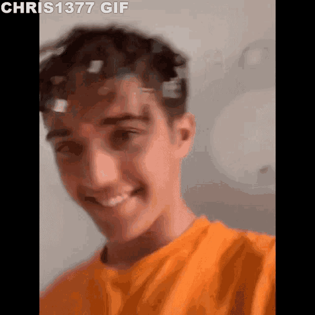 a young man in an orange shirt is smiling and making a face .
