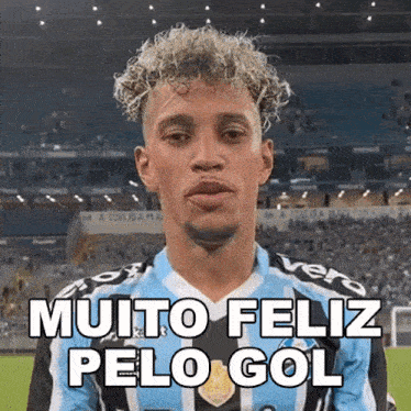 a man with curly hair is wearing a blue and black jersey that says muito feliz pelo gol