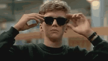a young man wearing sunglasses is adjusting his sunglasses in a library .