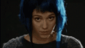 a woman with blue hair is looking at the camera with a serious look on her face .