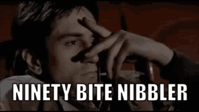 a man is sitting in a movie theater with his hand on his forehead and the words `` ninety bite nibbler '' .