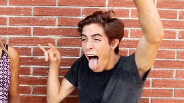 a man sticking his tongue out in front of a red brick wall