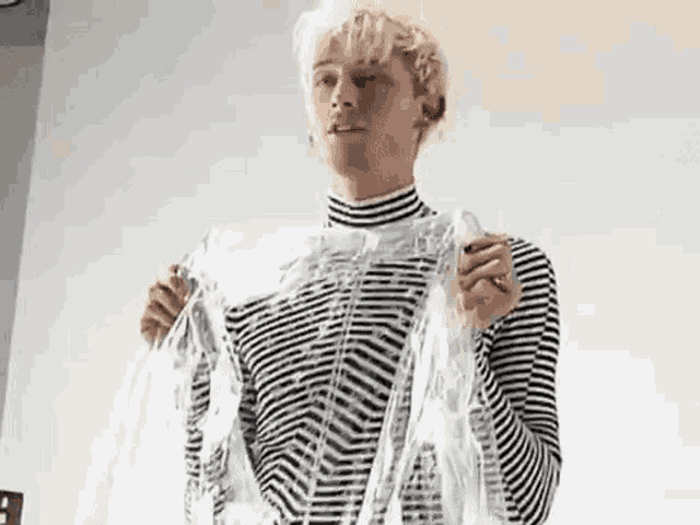 a young man in a striped shirt is holding a clear plastic bag .