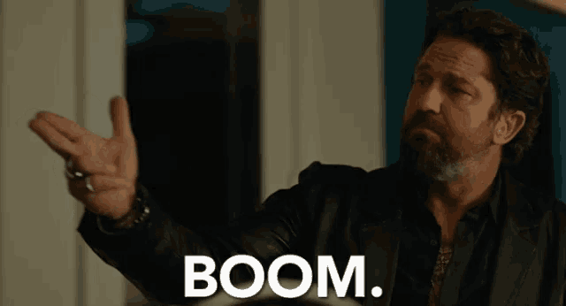a man with a beard and a black jacket is making a funny face and says boom .