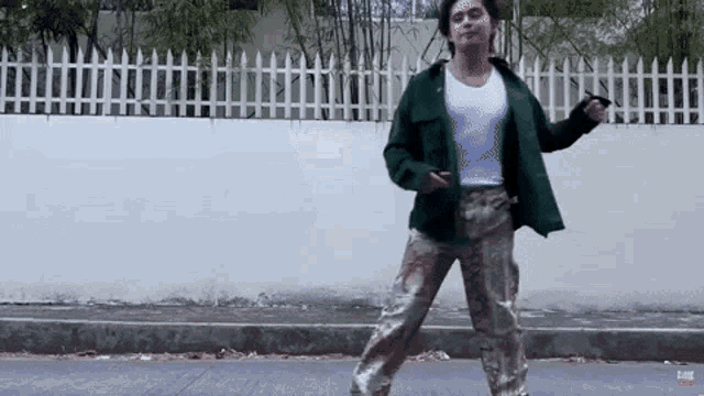 a man in a green jacket and camo pants is dancing on a street