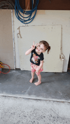 a little girl wearing a black shirt with a teddy bear on it gives the peace sign