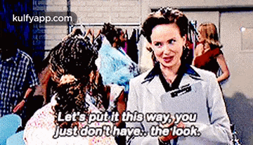 a woman in a white coat is talking to another woman in front of a clothes rack .