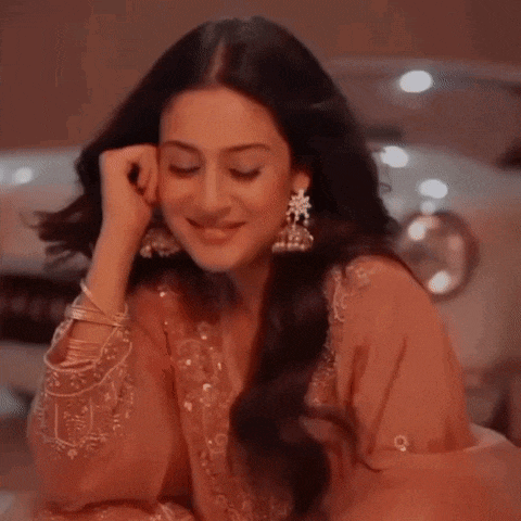 a woman in a pink dress and earrings is sitting in front of a car .