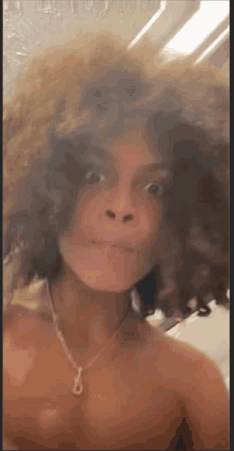 a woman without a shirt is taking a selfie in front of a mirror with her hair blowing in the wind .