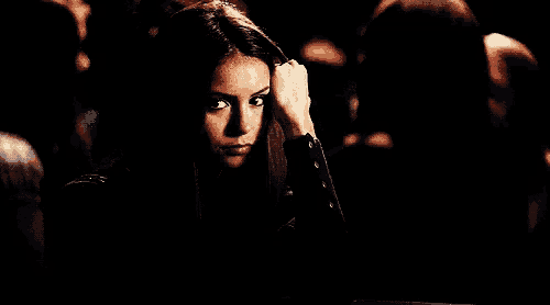 a woman is sitting in a dark room with her hands folded in front of her .