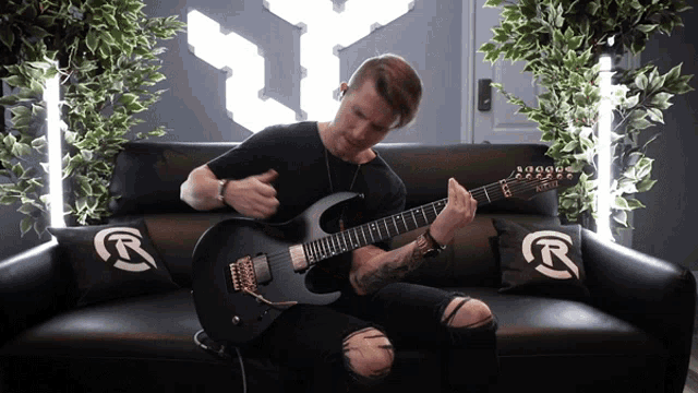a man is playing a guitar on a couch with a r on the pillow