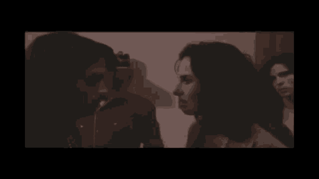 two women are talking to each other in a dark room with a picture on the wall behind them