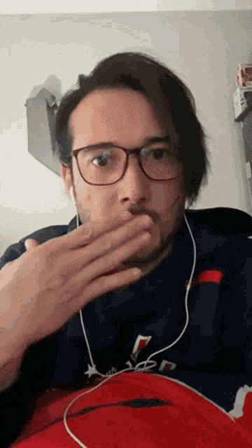 a man wearing glasses and ear buds covering his mouth with his hand