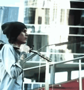 a man in a beanie is singing into a microphone while holding a violin