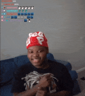 a young man wearing a red supreme hat is sitting on a couch