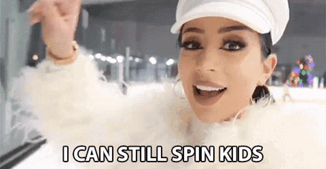 a woman in a white fur coat and hat is standing on an ice rink and says `` i can still spin kids '' .
