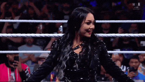 a woman in a black dress is standing in a wrestling ring
