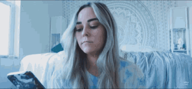 a woman sitting on a bed looking at a cell phone with a blue background