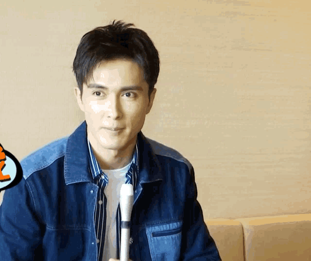 a man in a denim jacket holds a microphone in his right hand