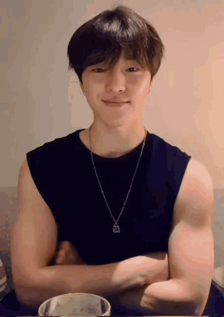 a young man is sitting at a table with his arms crossed and wearing a necklace .