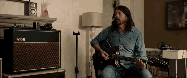 a man playing a guitar in front of a vox amp