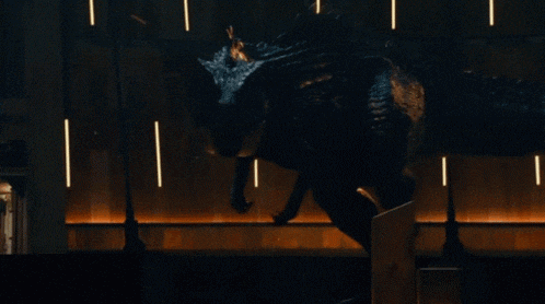 a large black dinosaur is standing in a dark room with lights behind it