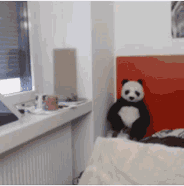a stuffed panda bear is sitting on a bed in a bedroom